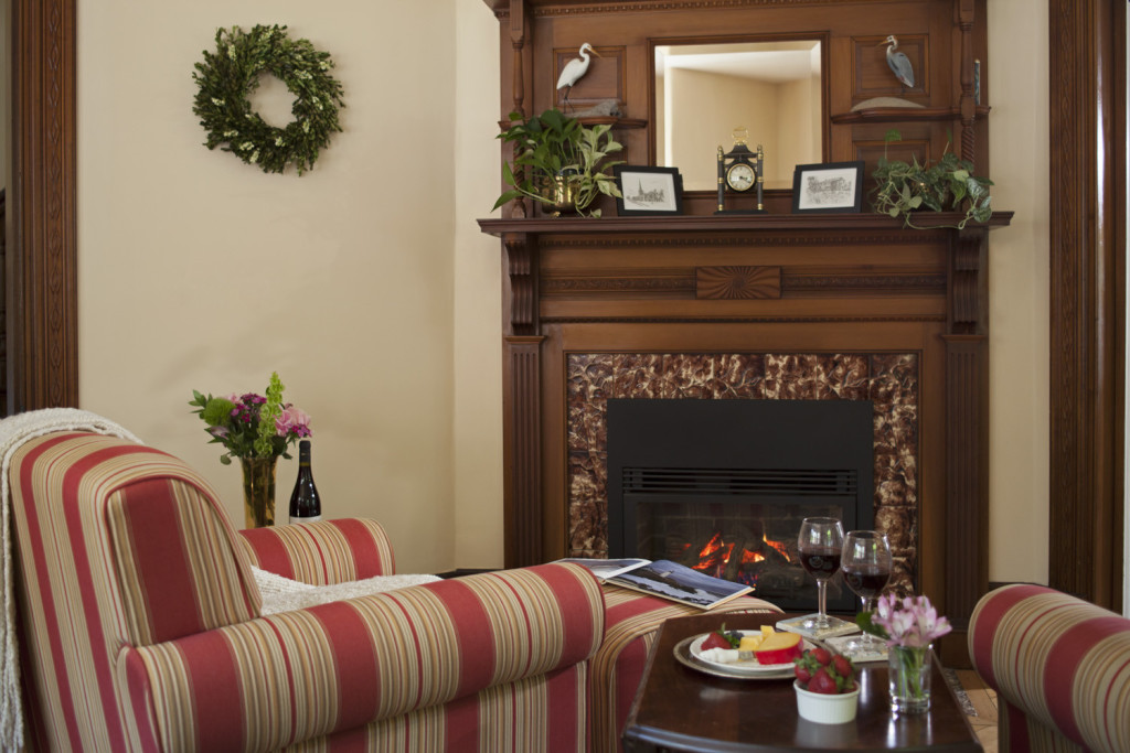 carved mahogony mantelpiece behind esy chair, wine glasses on a table and a fire buring in the fireplace