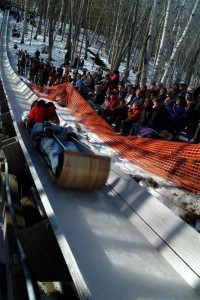 toboggan team heading downhill in an iced chute with crowd in background