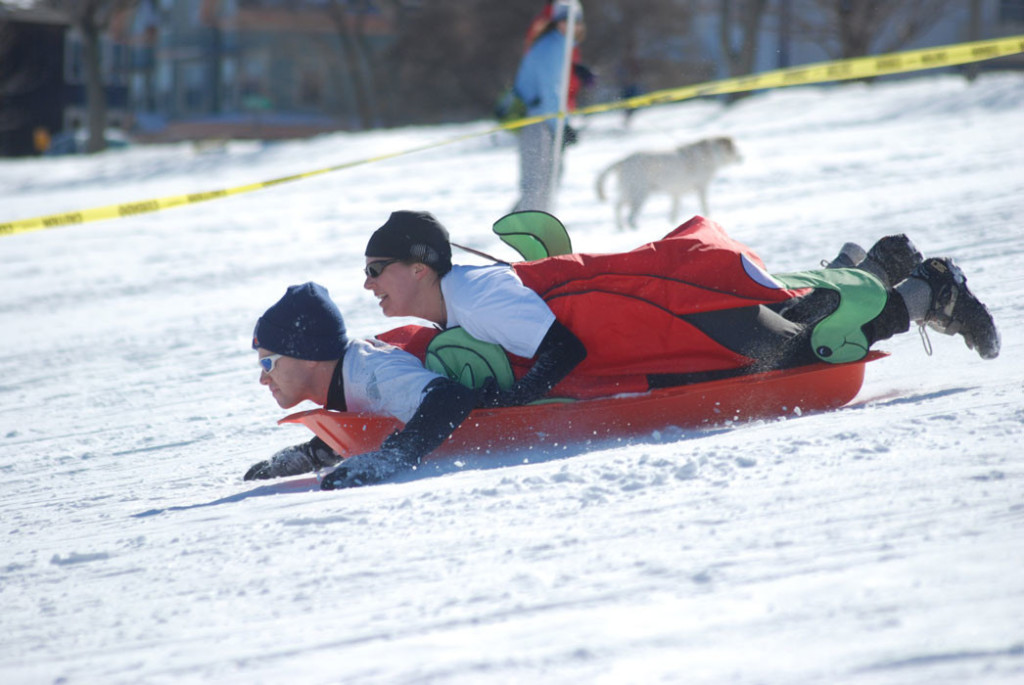 2 people racing downhill on a red plastic sled