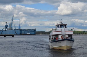 excursion boat heading upriver with shipyard in the background