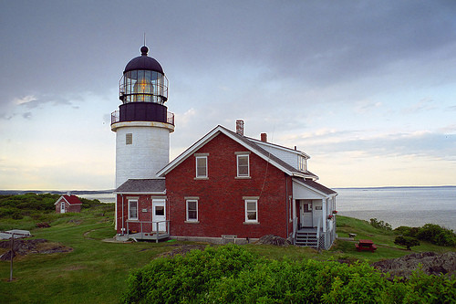 white lighthouse with red house on green grass with sea to rear