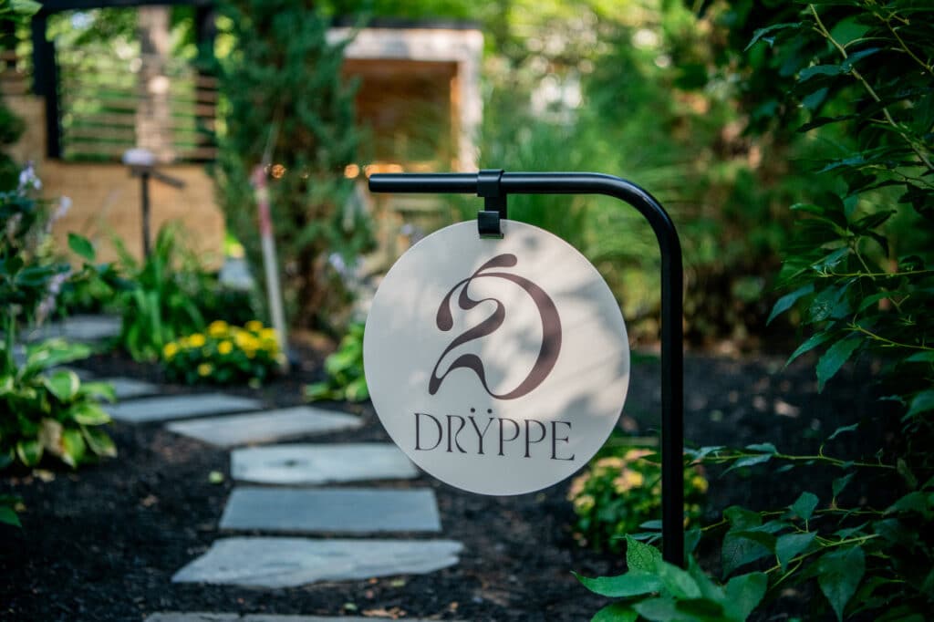 Dryppe sign in front of winding path leading to sauna & cold plunge setting surrounded by trees