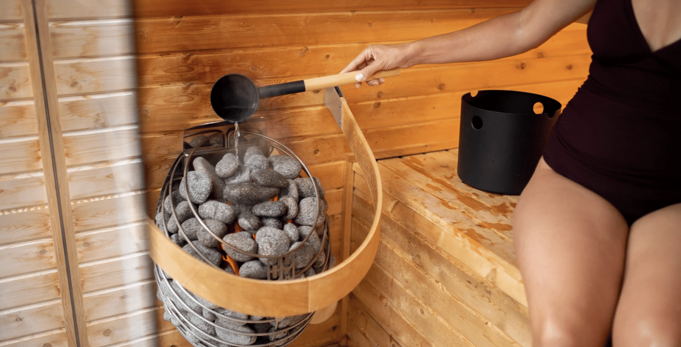 Guest pouring water over hot stones inside a wooden dry sauna at Brewster House Bed & Breakfast