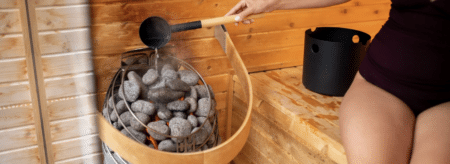 Guest pouring water over hot stones inside a wooden dry sauna at Brewster House Bed & Breakfast