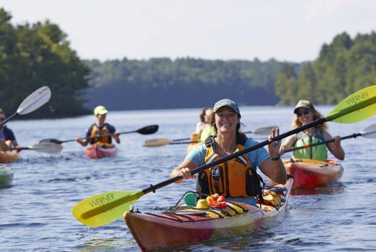 Multiple ladies smiling and kayaking on the water