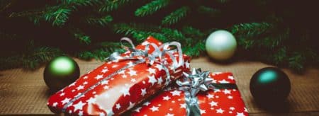 Two packages wrapped in red paper with white stars and silver ribbon under evergreen