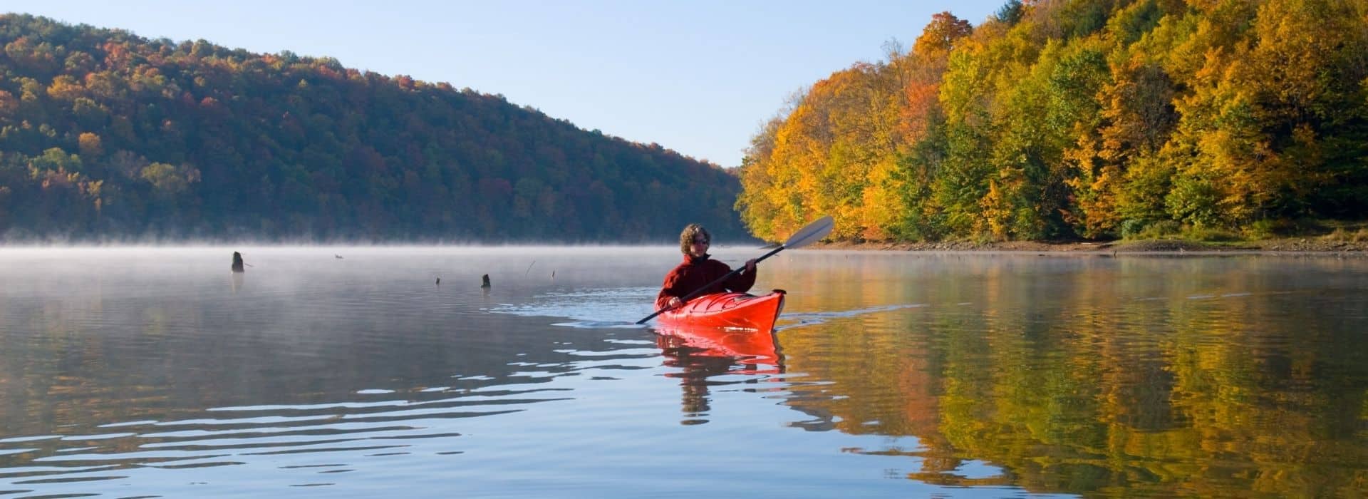 kayaker on calm waters with fall foliage all around