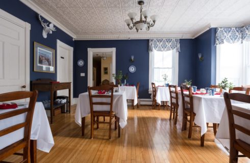 Large dining room with hardwood floors, dark blue walls, white trim, and multiple wooden tables covered with white tablecloths