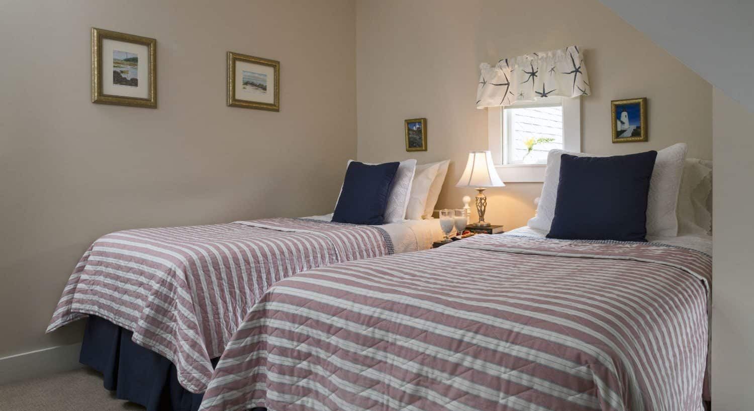 Bedroom with light cream walls, white trim, and two twin beds with light pink, white and navy bedding