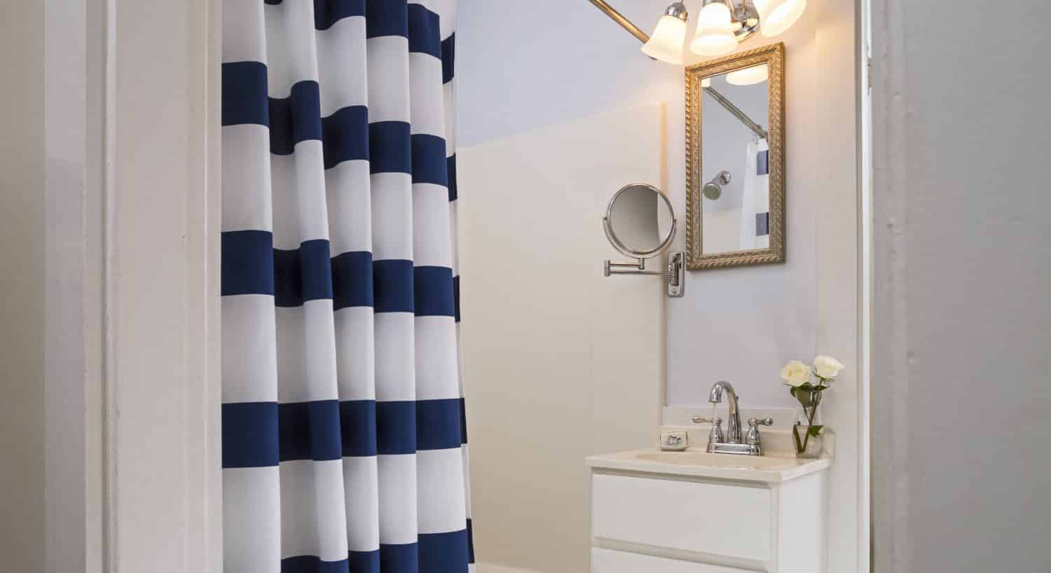Bathroom with white vanity, cream sink, ornate mirror, and white and navy striped shower curtain