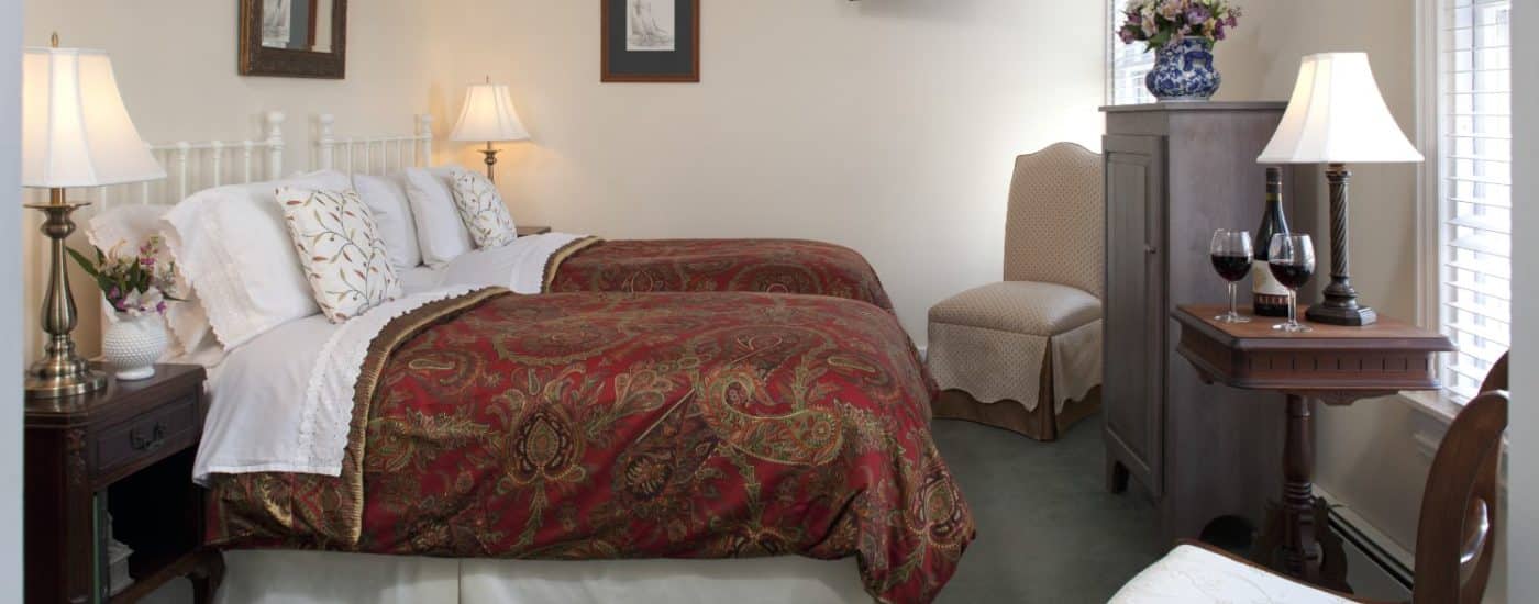 Large bedroom with two twins bed, white painted wrought iron headboard red and gold paisley bedding, and wooden furniture