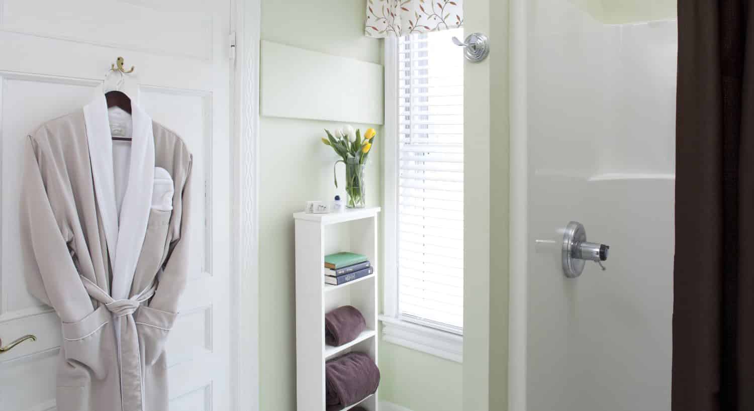 Bathroom with stand up shower, light lime green walls, white trim, and tan robe hanging on a hook