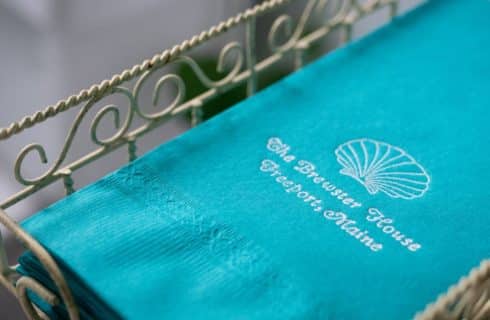 Close up view of turquoise napkins with The Brewster House Freeport, Maine text embossed in white