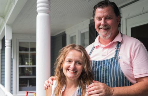 Man and woman wearing aprons standing on front porch of property