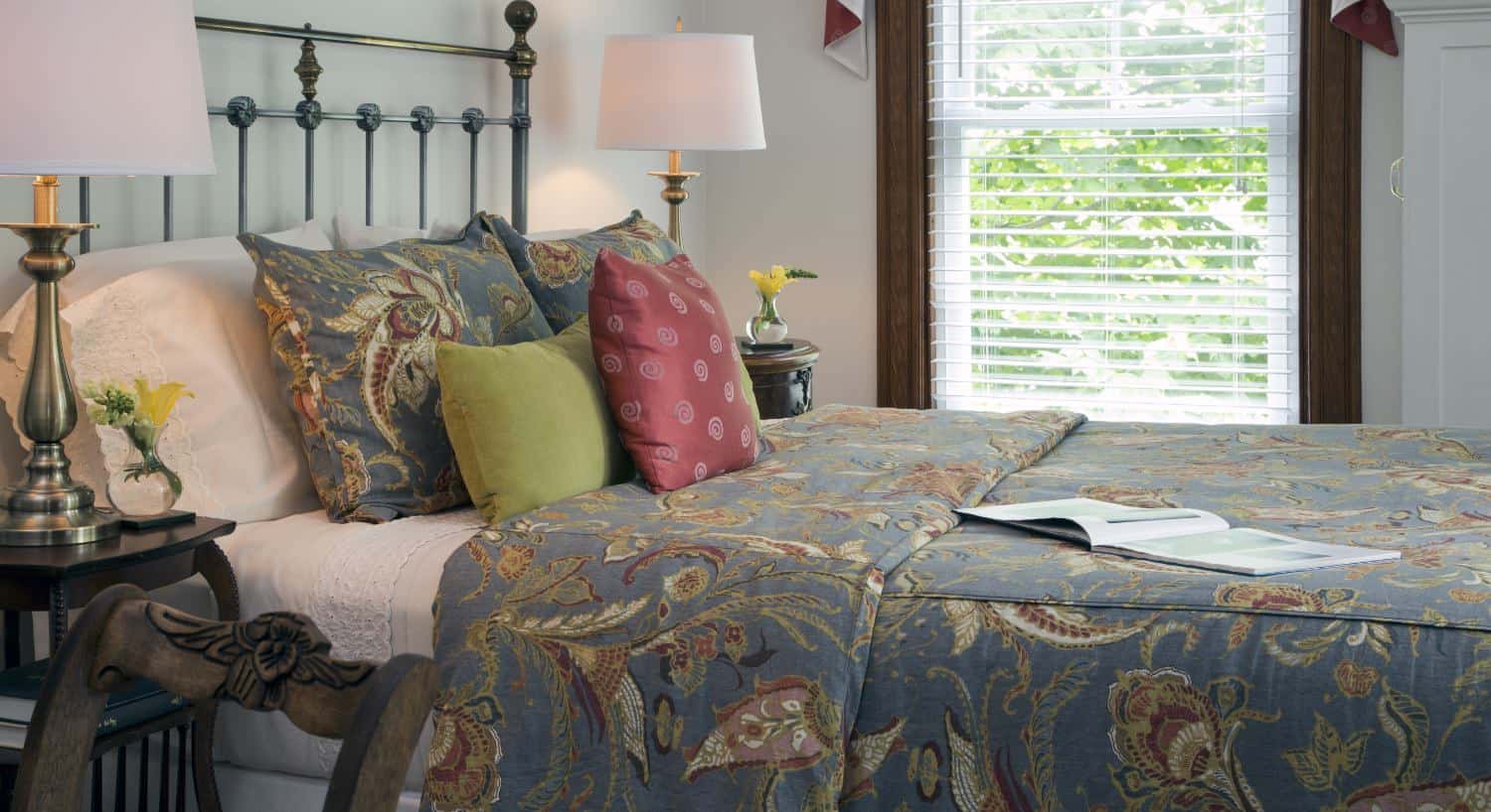 Bedroom with light-colored walls, dark wooden trim, blueish gray painted wrought iron headboard, and multicolored bedding