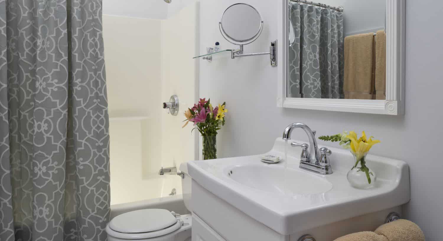 Bathroom with light gray walls, white sink, white vanity, gray and white shower curtain, and white-trimmed mirror