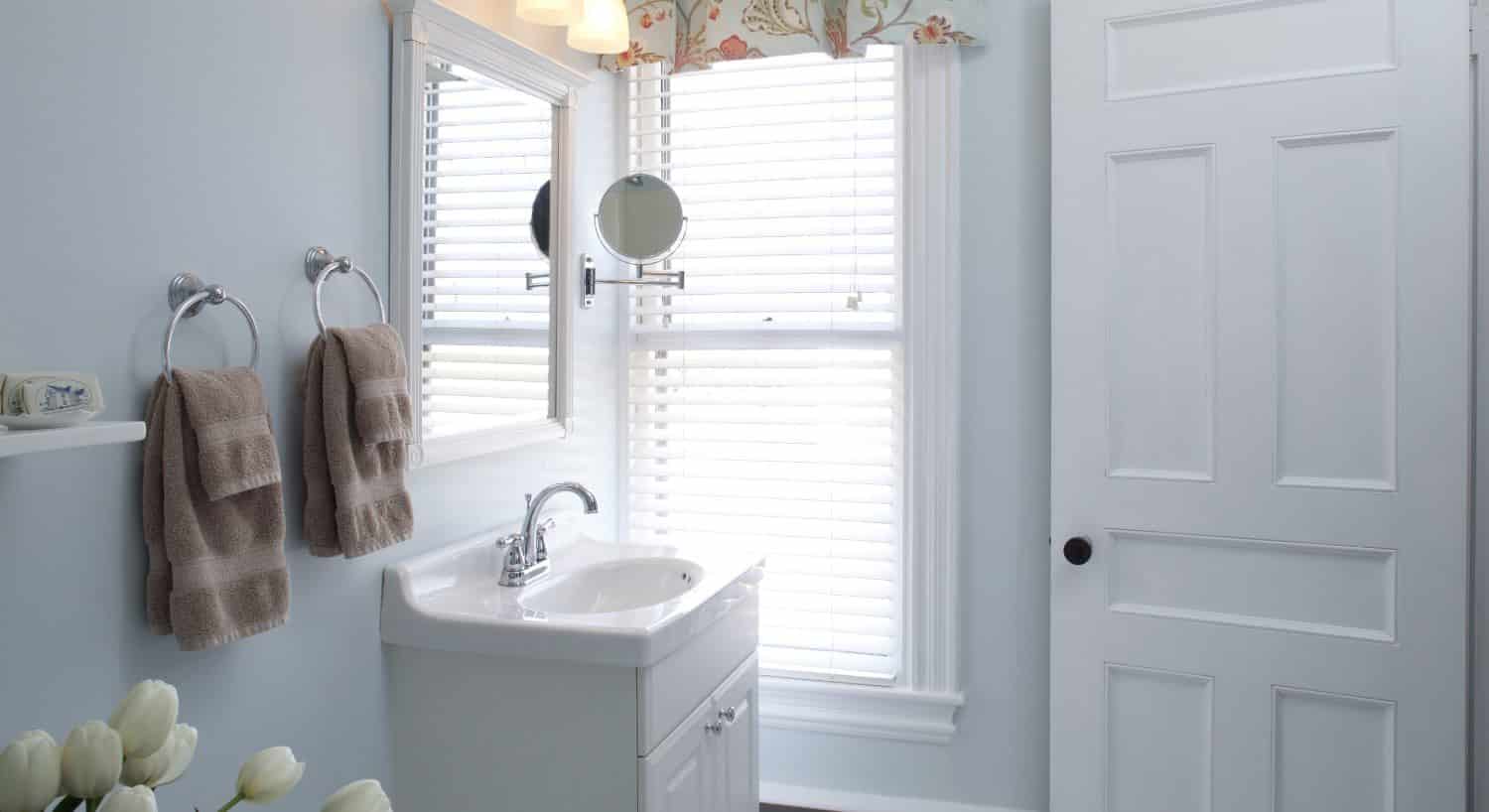 Bathroom with light blue walls, white vanity, white sink, and two hanging light brown sets of towels