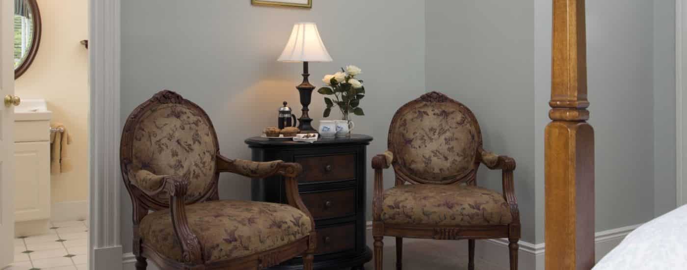 Bedroom with a sitting area, two antique wooden chairs with cushions, and small dark wooden dresser