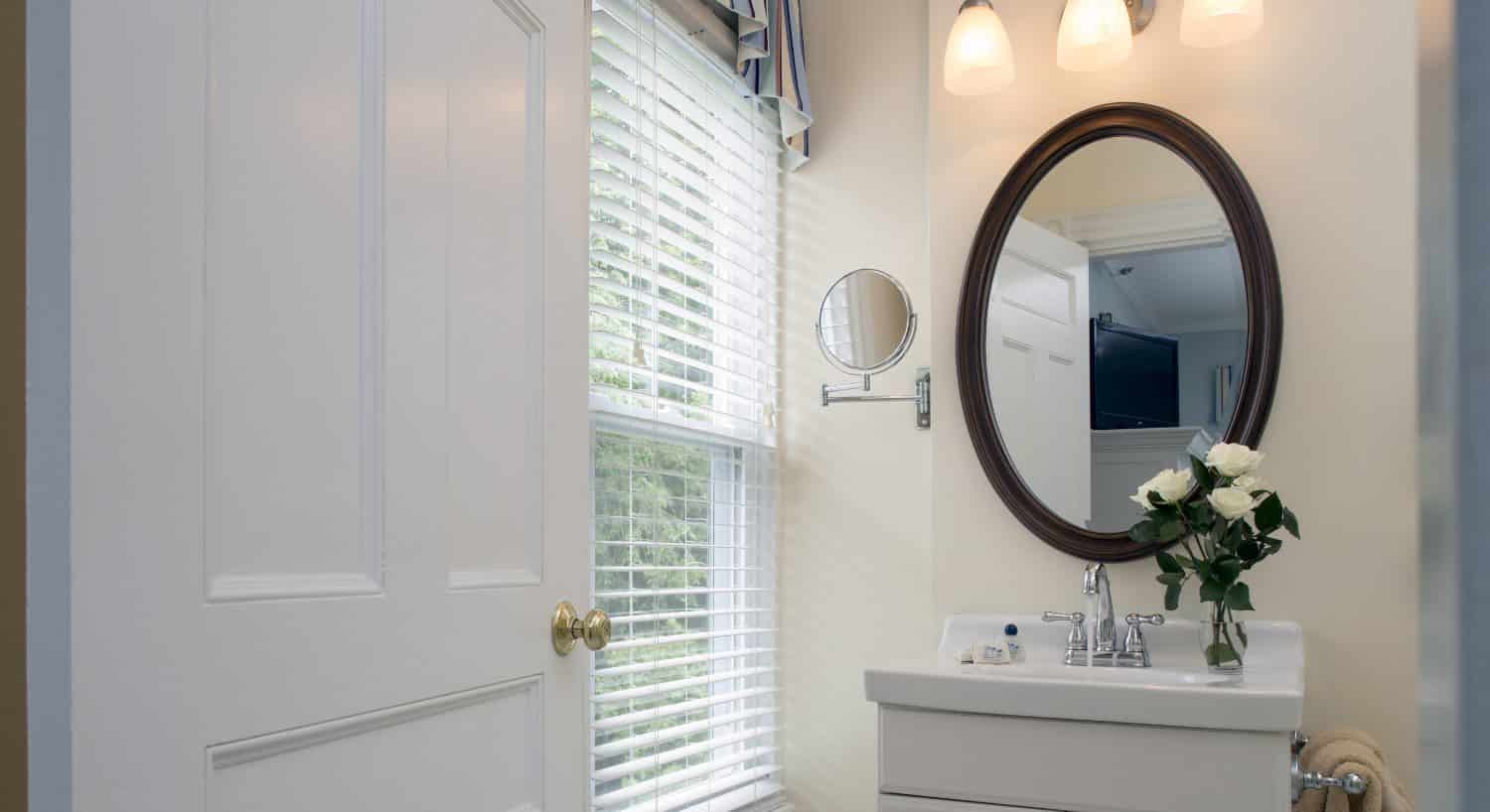 Bathroom with light cream walls, white sink, white vanity, and large oval mirror with dark brown trim