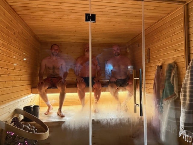 3 guys on top bench of sauna. steamy window