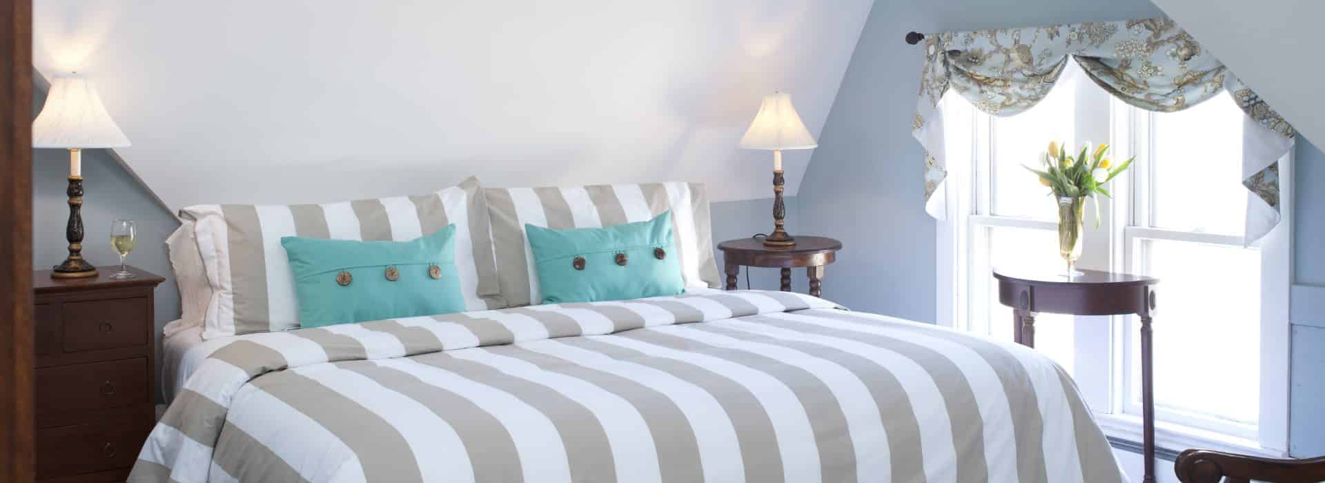 Bedroom with light gray-blue walls, white trim, taupe and white striped bedding, turquoise accent pillows, and dark wooden furniture