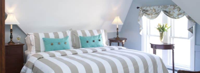 Bedroom with light gray-blue walls, white trim, taupe and white striped bedding, turquoise accent pillows, and dark wooden furniture
