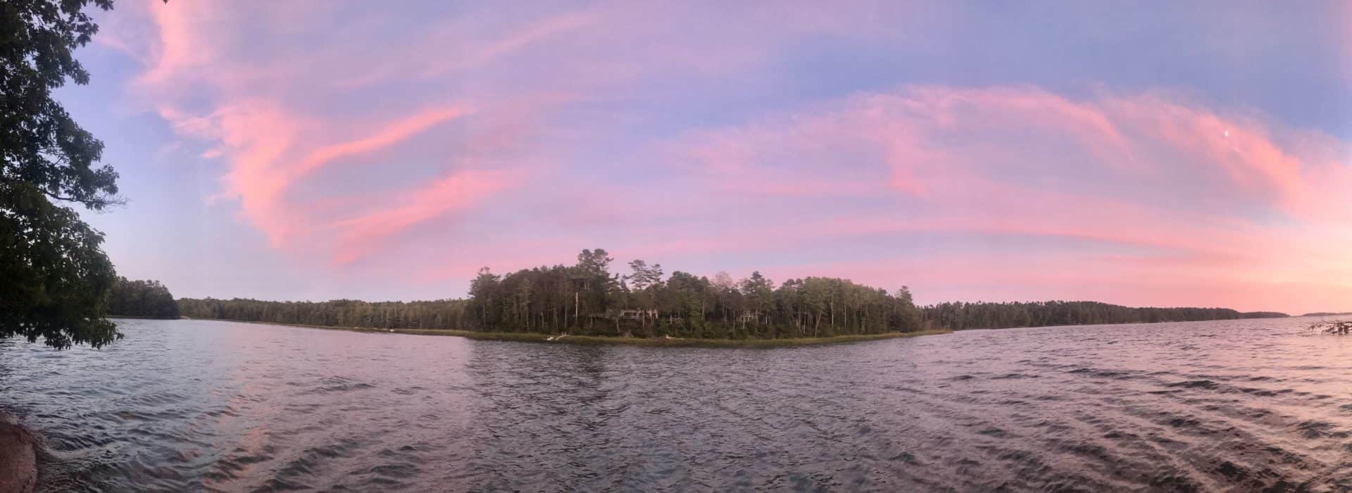 View of mostly calm water with island of trees in the background at dusk