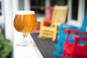 Close up view of a glass filled with light colored beer and colorful wooden rocking chairs blurred in the background
