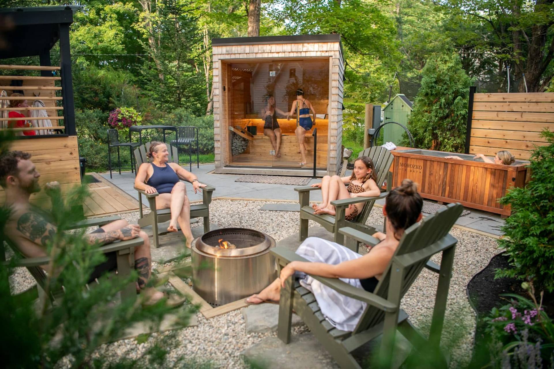 Group enjoying sauna, cold plunge and firepit in backyard experience called Dryppe