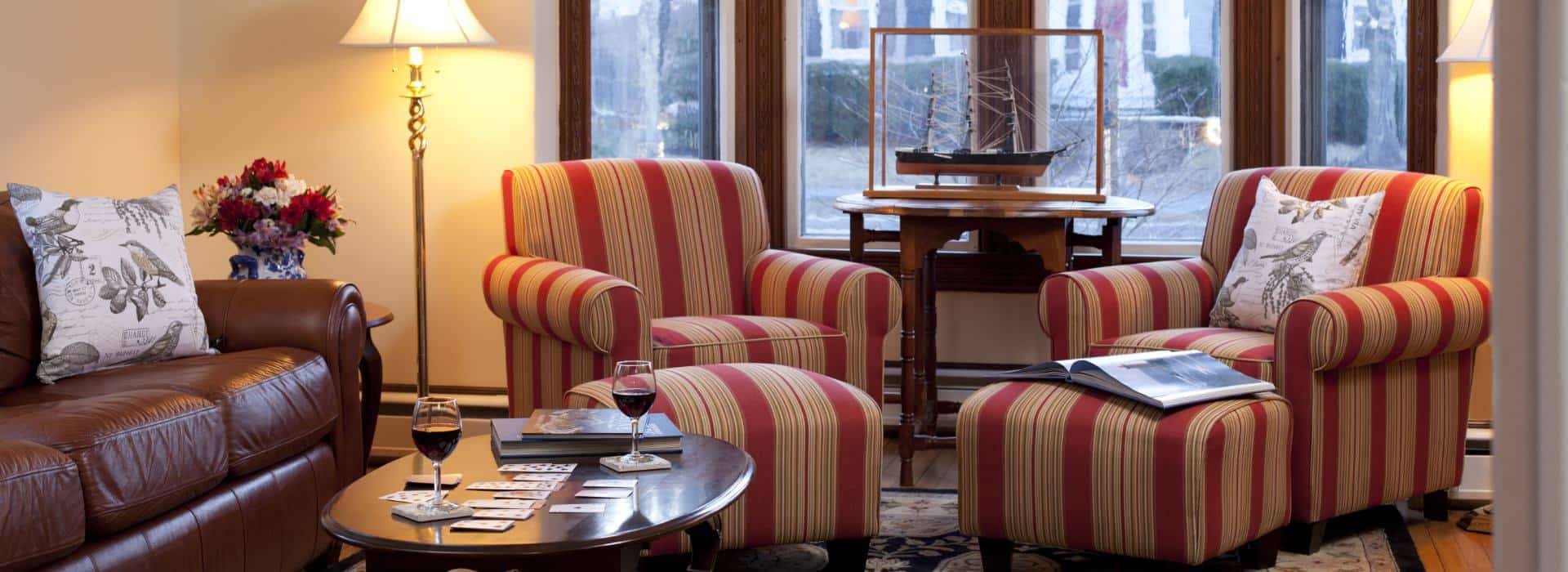 Cozy guest lounge at Brewster House Bed & Breakfast in Freeport, Maine, featuring warm lighting, striped armchairs, and a relaxing atmosphere